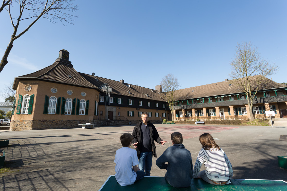 Ein Mann im Gespräch mit drei Kindern auf dem Schulhof eines Leuchtturmprojekts der Anneliese Brost-Stiftung